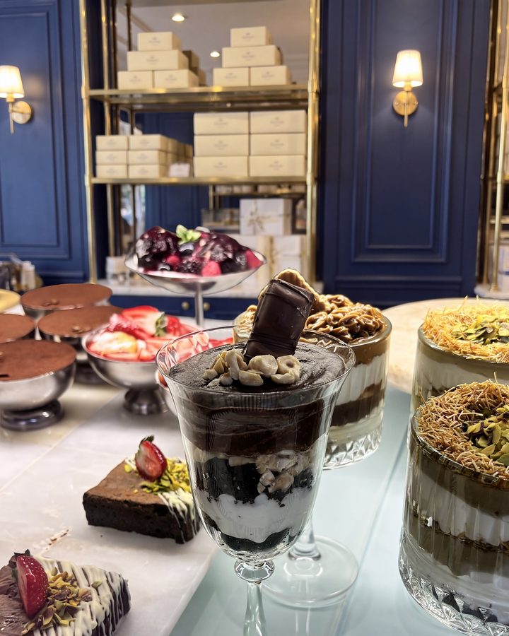 Lacivert boiserie duvarlı pastanede cam vitrin: kat kat cup'lar, browni dilimleri ve raflarda Lavaly kutuları